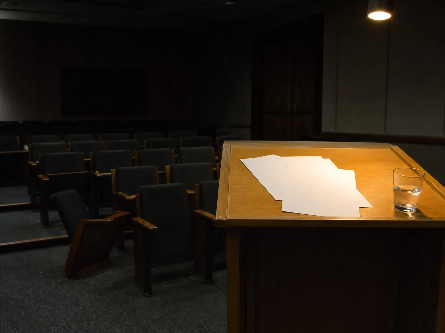Empty lecture hall with a lit wooden lectern holding blank papers and a glass of water