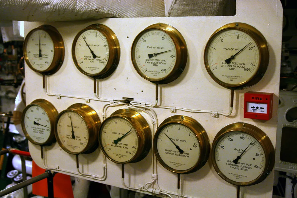 Brass-rimmed tank-level gauges in HMS Belfast's engine room, graduated in tons of water