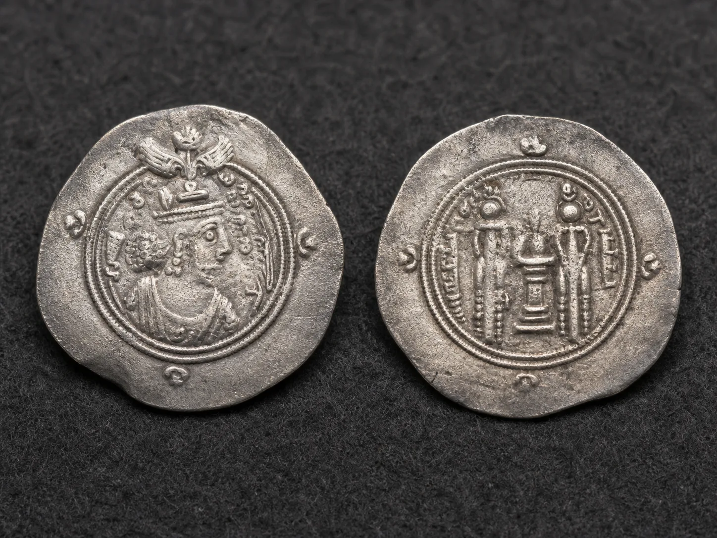 Two sides of a worn silver Sasanian coin showing a crowned bust and fire altar on dark cloth